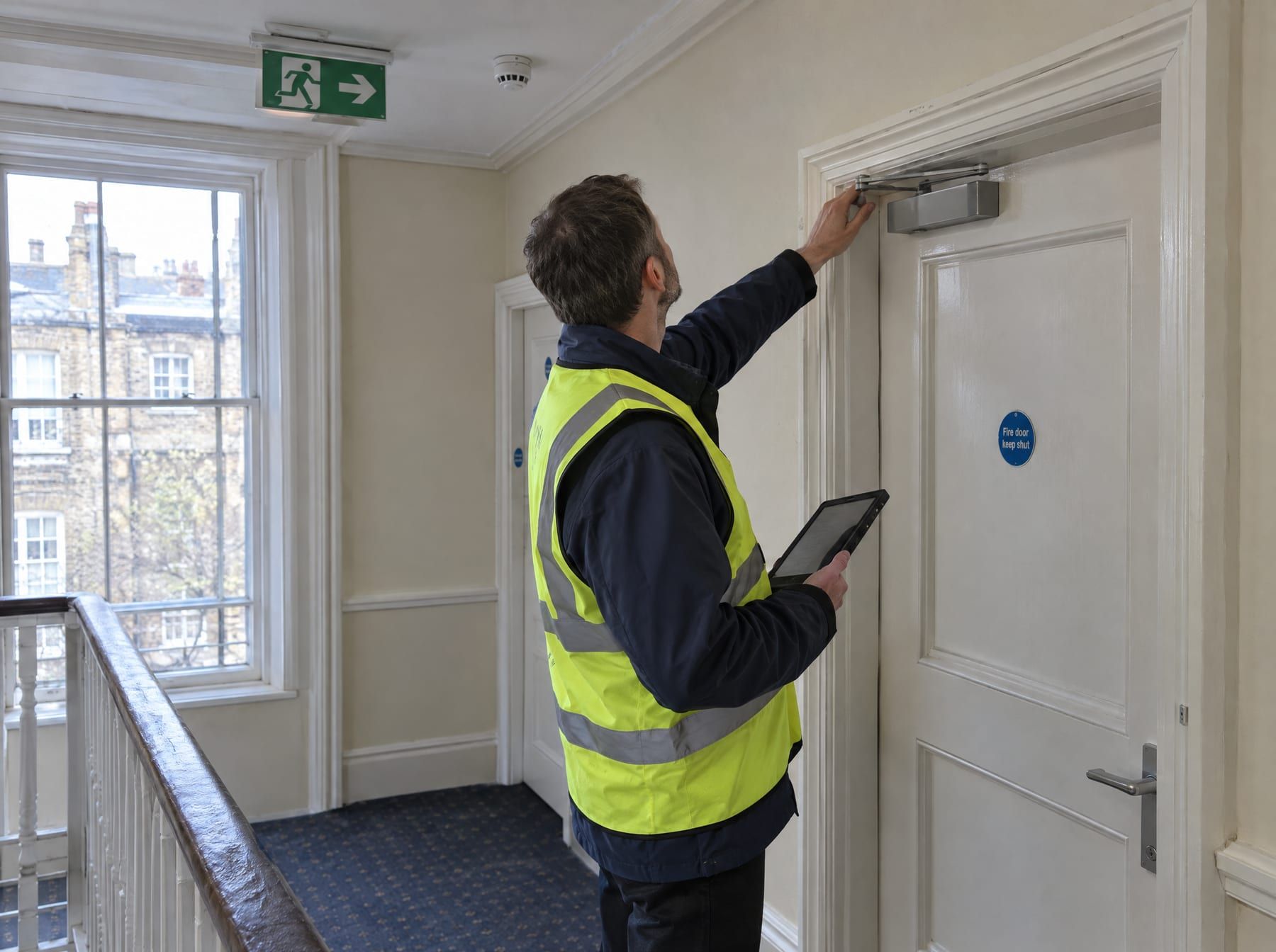 Fire risk assessor checking a communal fire door and its self-closer in a London block of flats